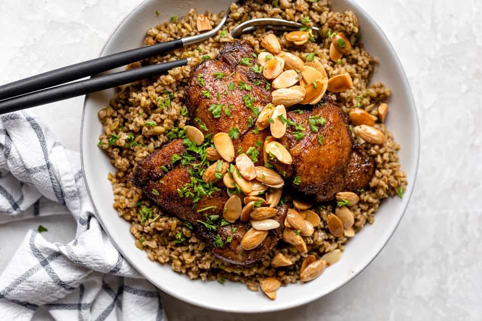 Freekah with chicken on a serving dish with serving utensil.