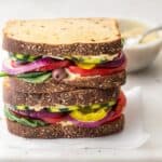 Veggie and hummus sandwiches stacked on top of each other with small bowl of hummus in background
