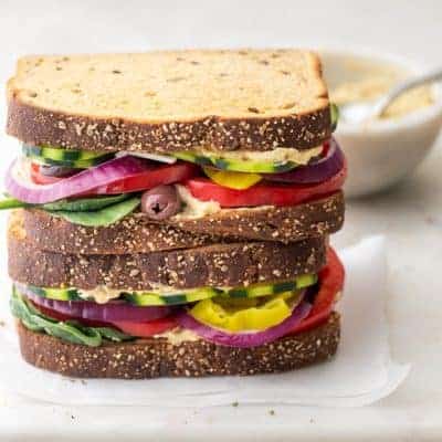 Veggie and hummus sandwiches stacked on top of each other with small bowl of hummus in background