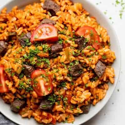 Jollof rice served in a bowl with beef and tomatoes on top