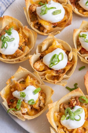 Close up of taco cups with chicken, cheese, sour cream and green onions.