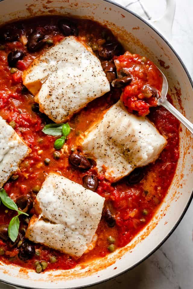 Spoon showing the tomato sauce with the poached cod