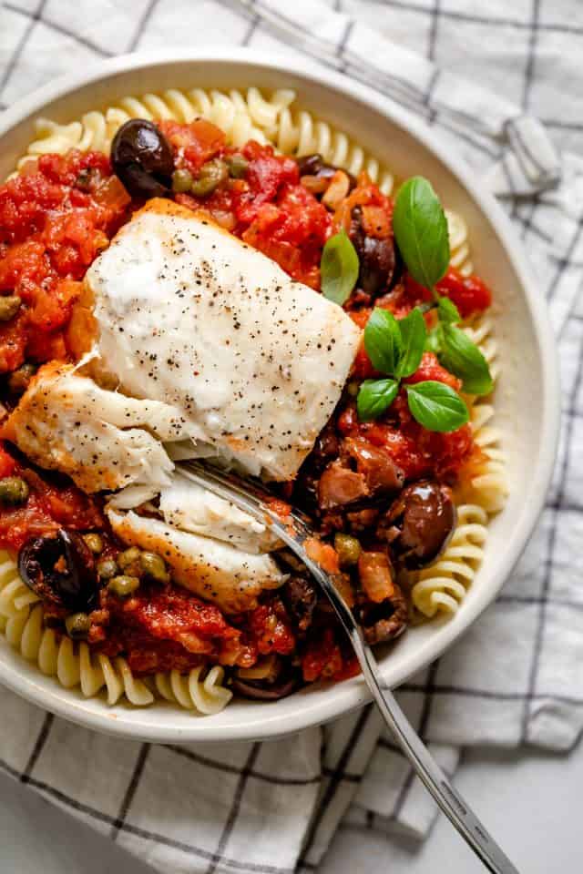 Piece of the poached fish served over the tomato sauce along with pasta in a small white bowl
