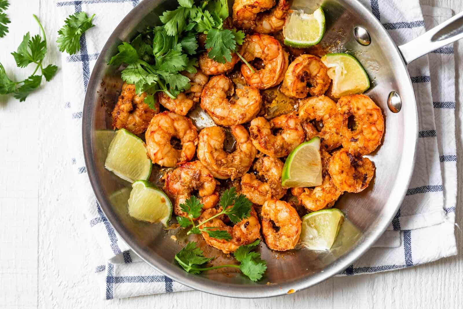 Chili lime shrimp in a pan with garnish and lime. 