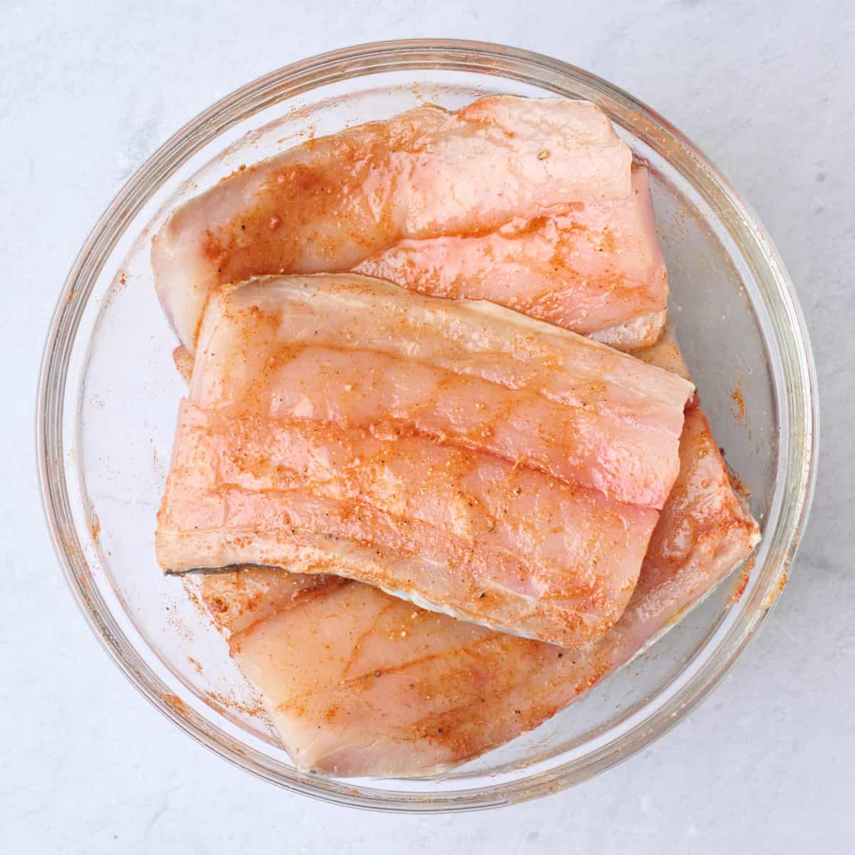 Fish in a bowl after seasoning and coating with oil.