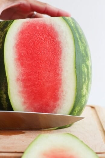 Large watermelon on cutting board with side part getting cut off.