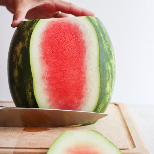 Large watermelon on cutting board with side part getting cut off.