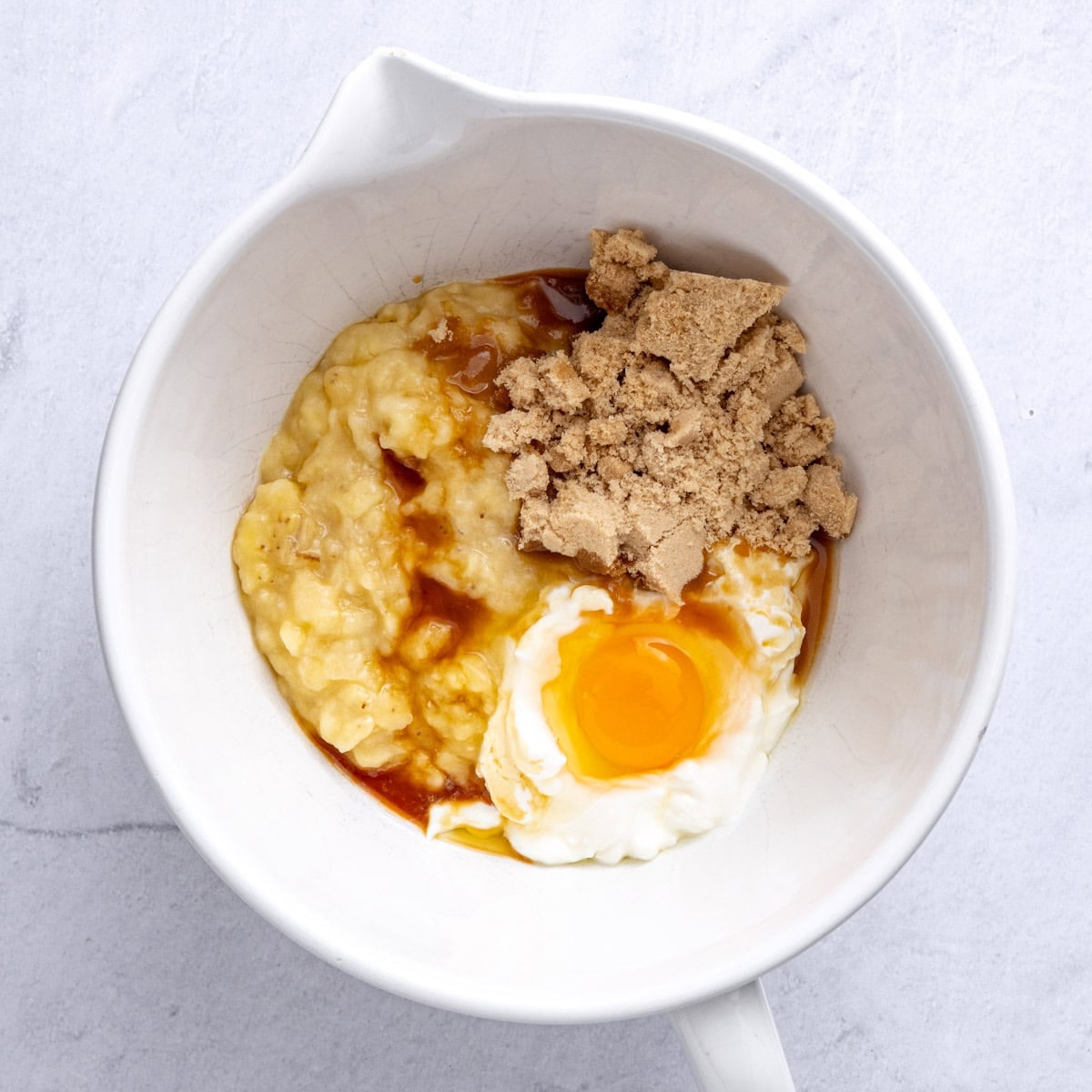 Mashed bananas, yogurt, egg, brown sugar and vanilla in a bowl before mixing.