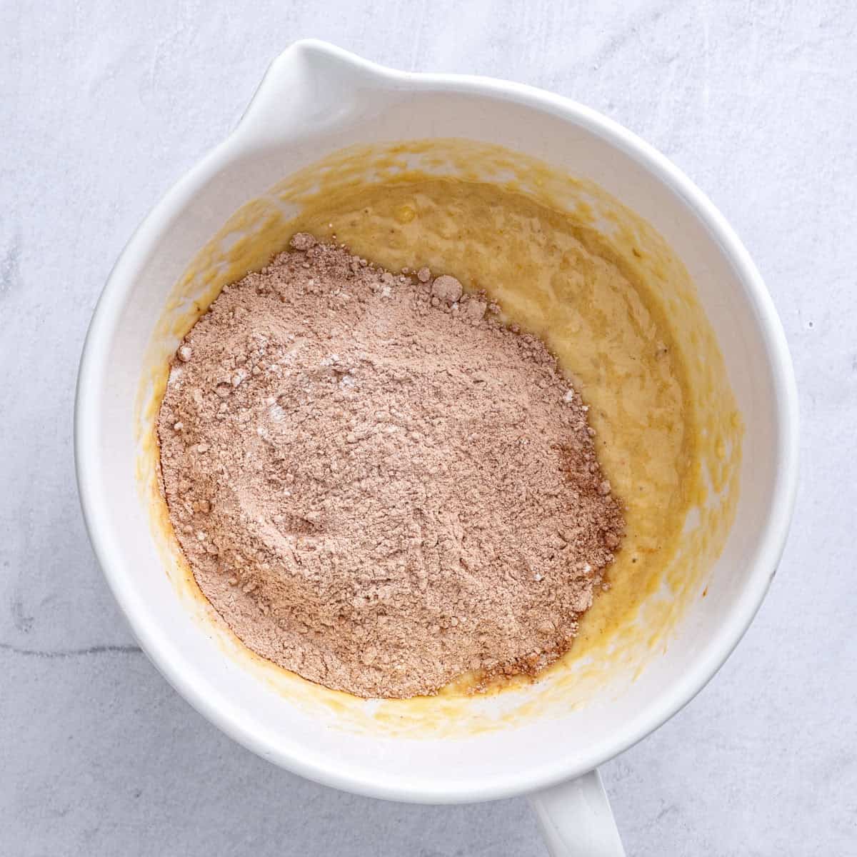 Mashed bananas, yogurt, egg, brown sugar and vanilla in a bowl after mixing with dry ingredients added.
