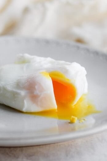 A poached egg broken so the yolk is coming out, on a plate.