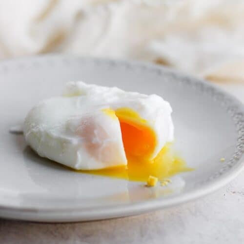 A poached egg broken so the yolk is coming out, on a plate.