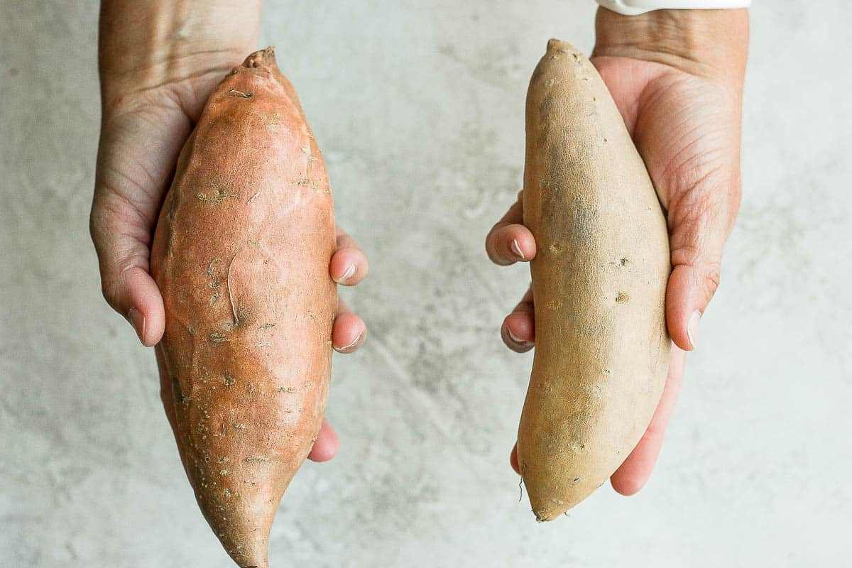 One hand holding sweet potato and another hand holding yam