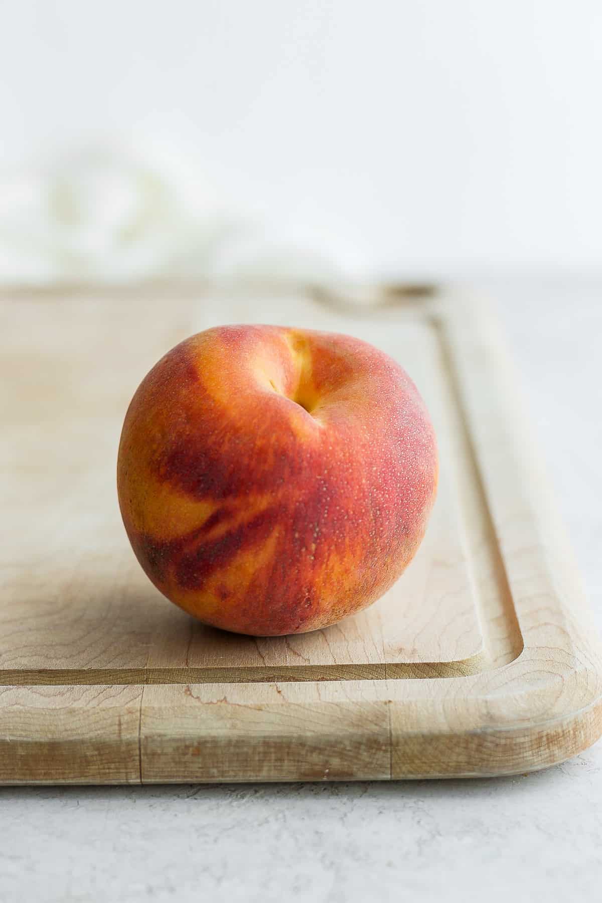 One ripe peach sitting on cutting board
