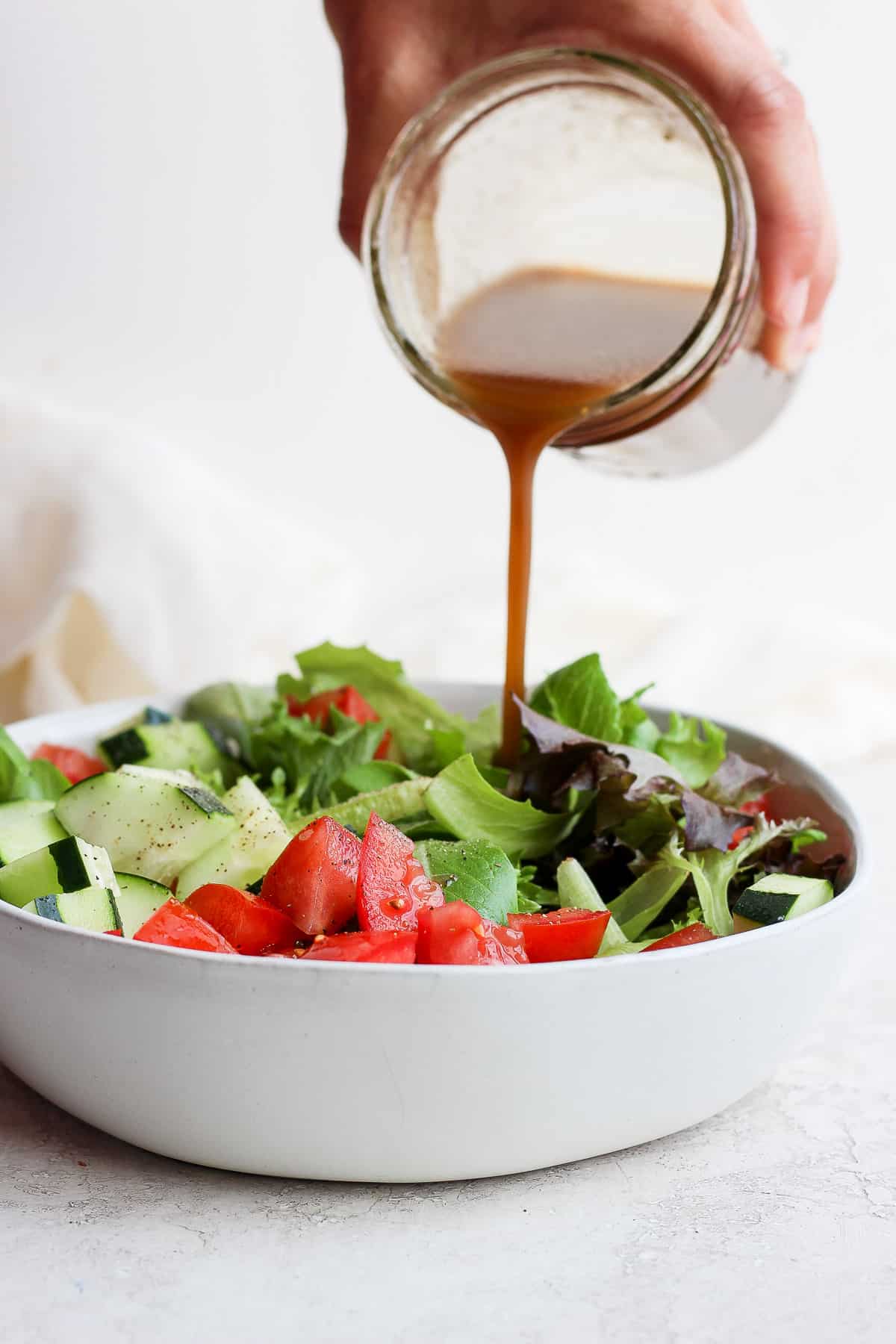 Homemade salad dressing getting poured over large bowl of salad