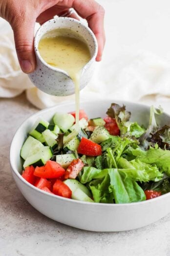 Homemade salad dressing getting poured over large bowl of salad