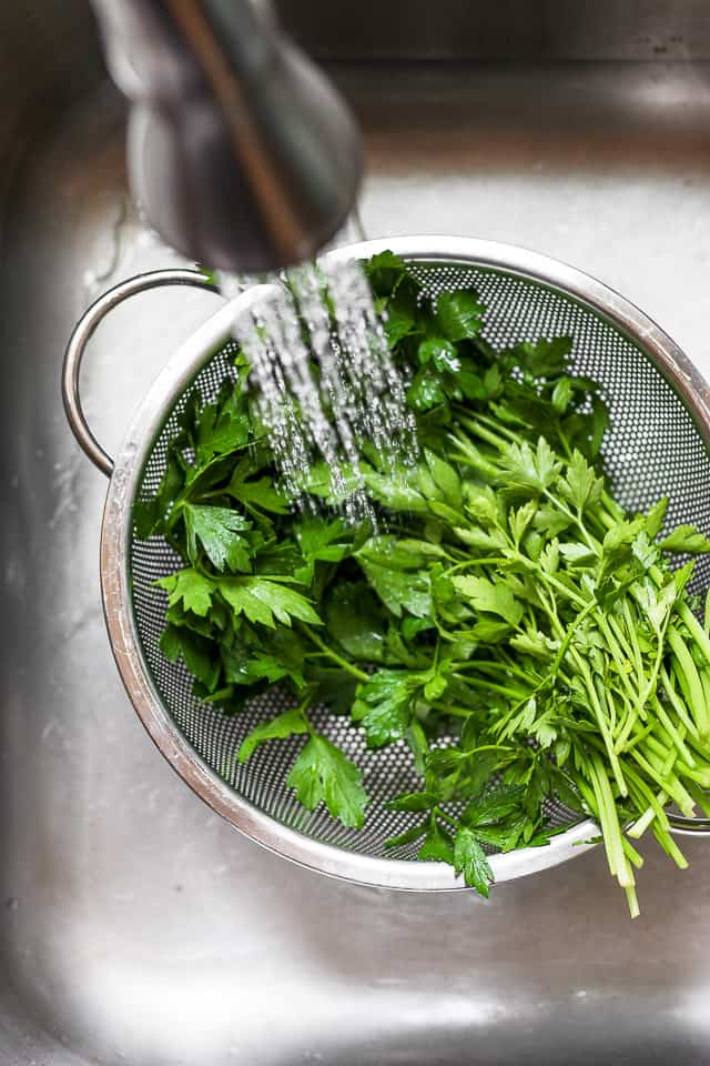 Bunch of parsley in colander getting rinsed with water in the sink