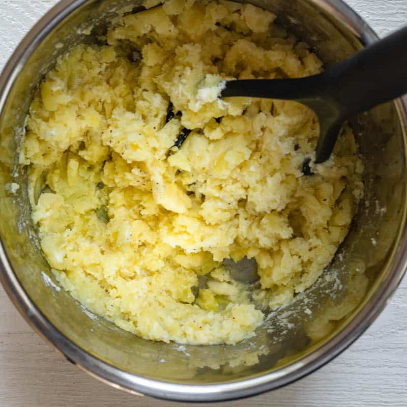 Potato masher resting in the bowl of mixed mashed potatoes.