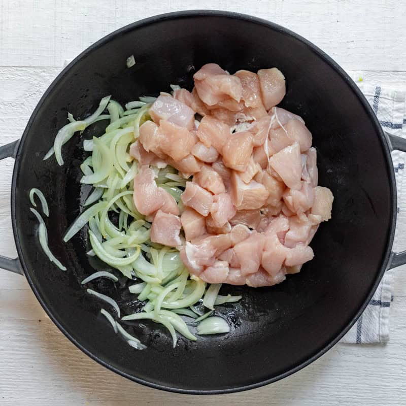 Raw chicken and onions in pot.