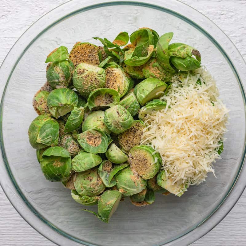 Brussels sprouts in a medium sized bowl with other ingredients before mixing.