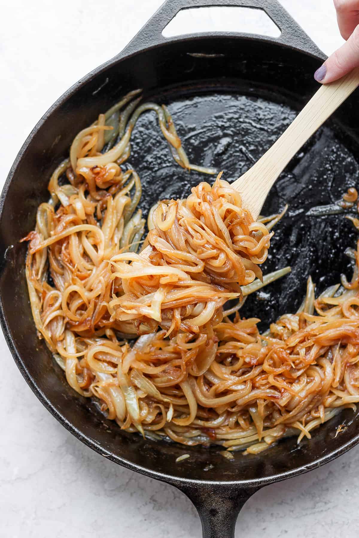 Wooden spoon scooping caramelized onions