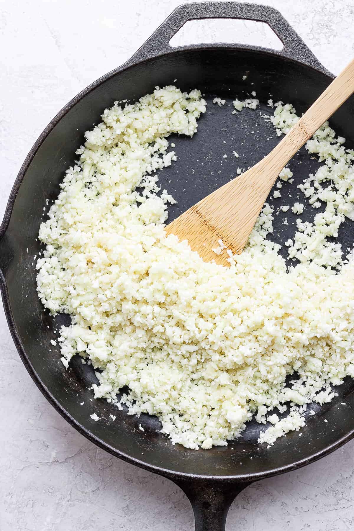 Cooking cauliflower rice in skillet with wooden spatula