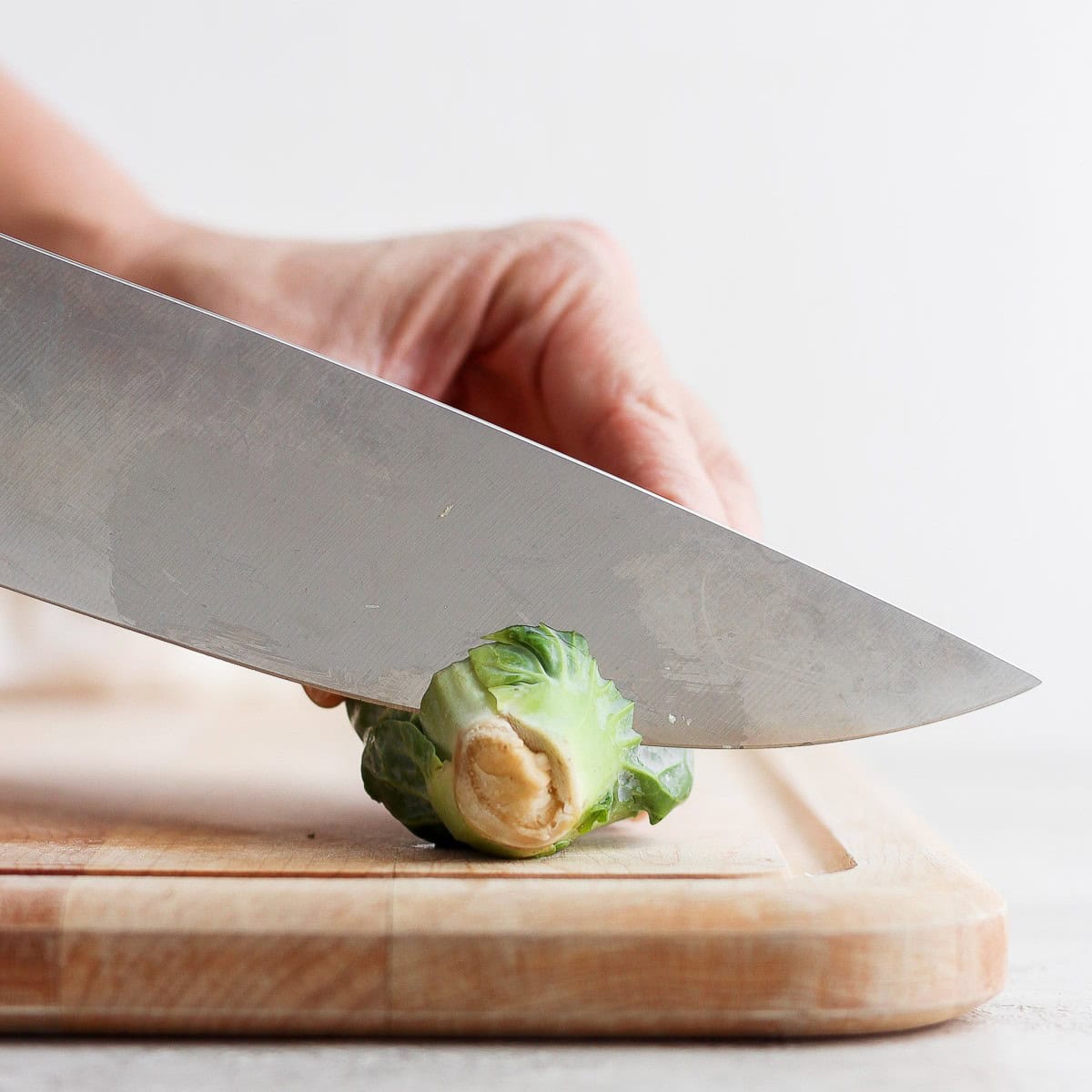 Using a sharp knife to remove ยผ inch of the stem of a brussel sprout.
