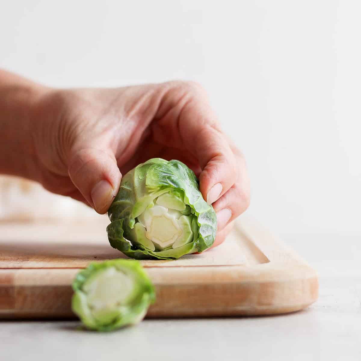 Using a sharp knife to remove ยผ inch of the stem of a brussel sprout.