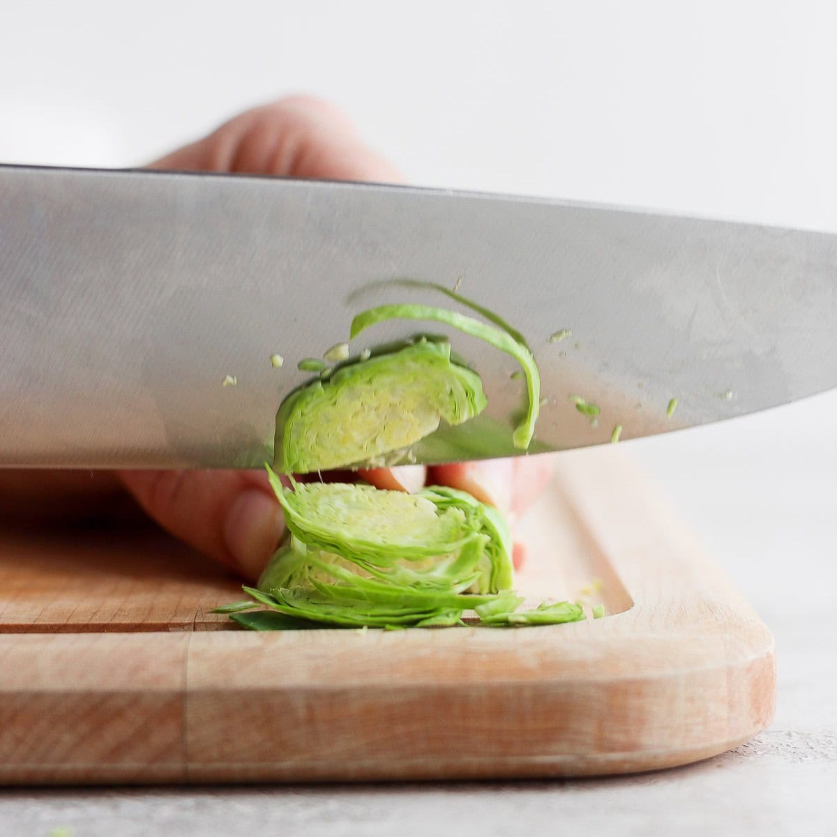Hand holding the sprout toward the stem end and making thin slices crosswise.