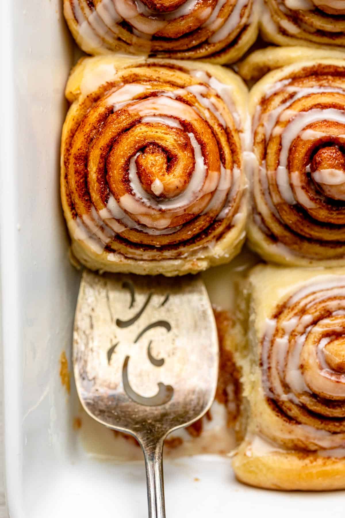 Spatula removing one cinnamon roll from pan