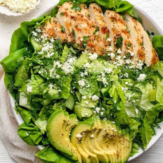 Green goddess salad in a large serving bowl with a small bowl of feta next to it.