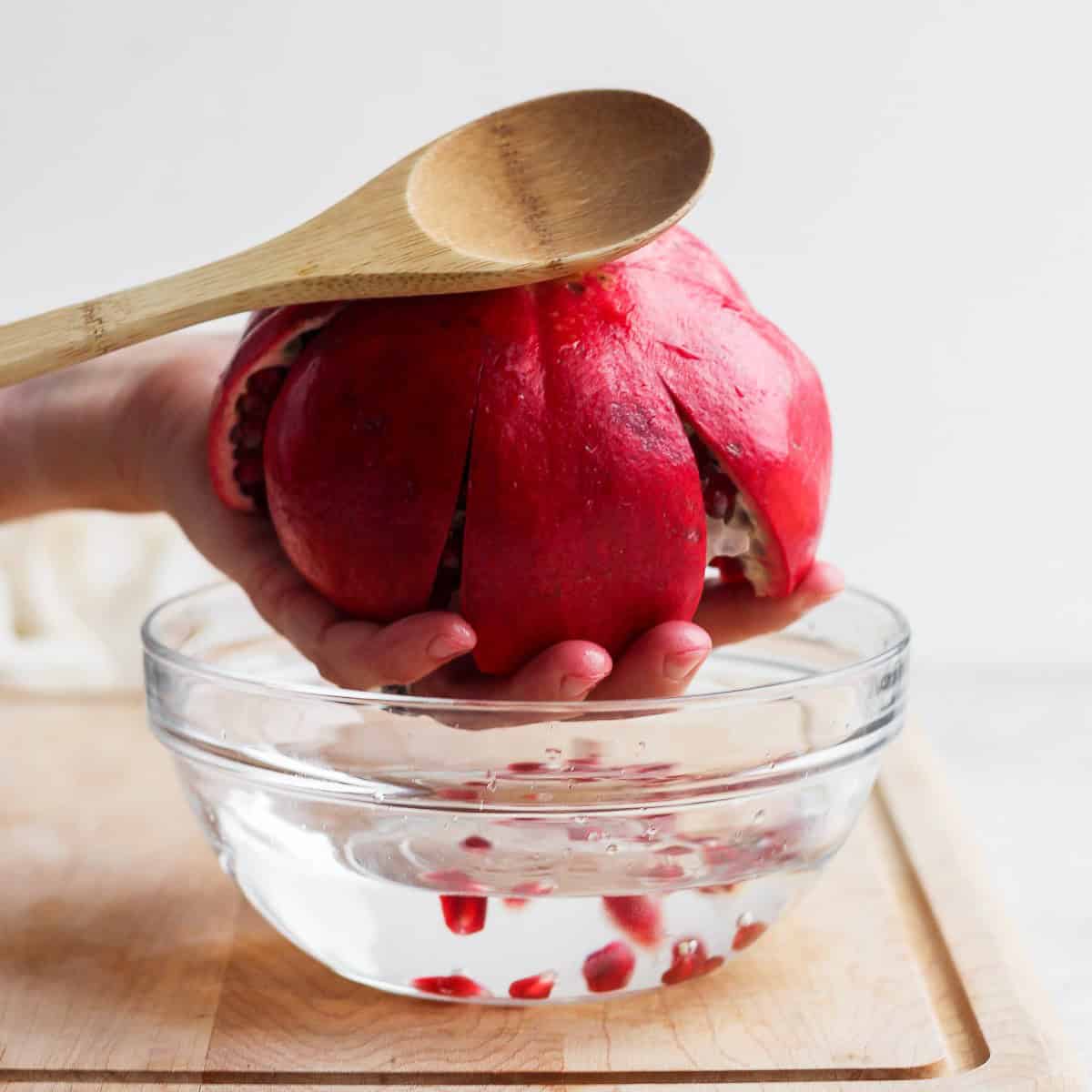 Hitting top of pomegranate with spoon to release seeds.