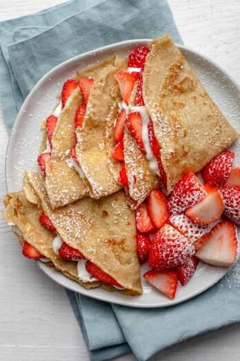 Overhead shot of protein crepes with strawberries and cream on blue napkin