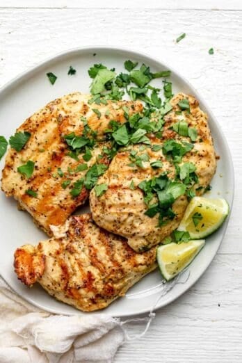 Plate of grilled chicken made with dijon marinade and served with lime wedges and cilantro