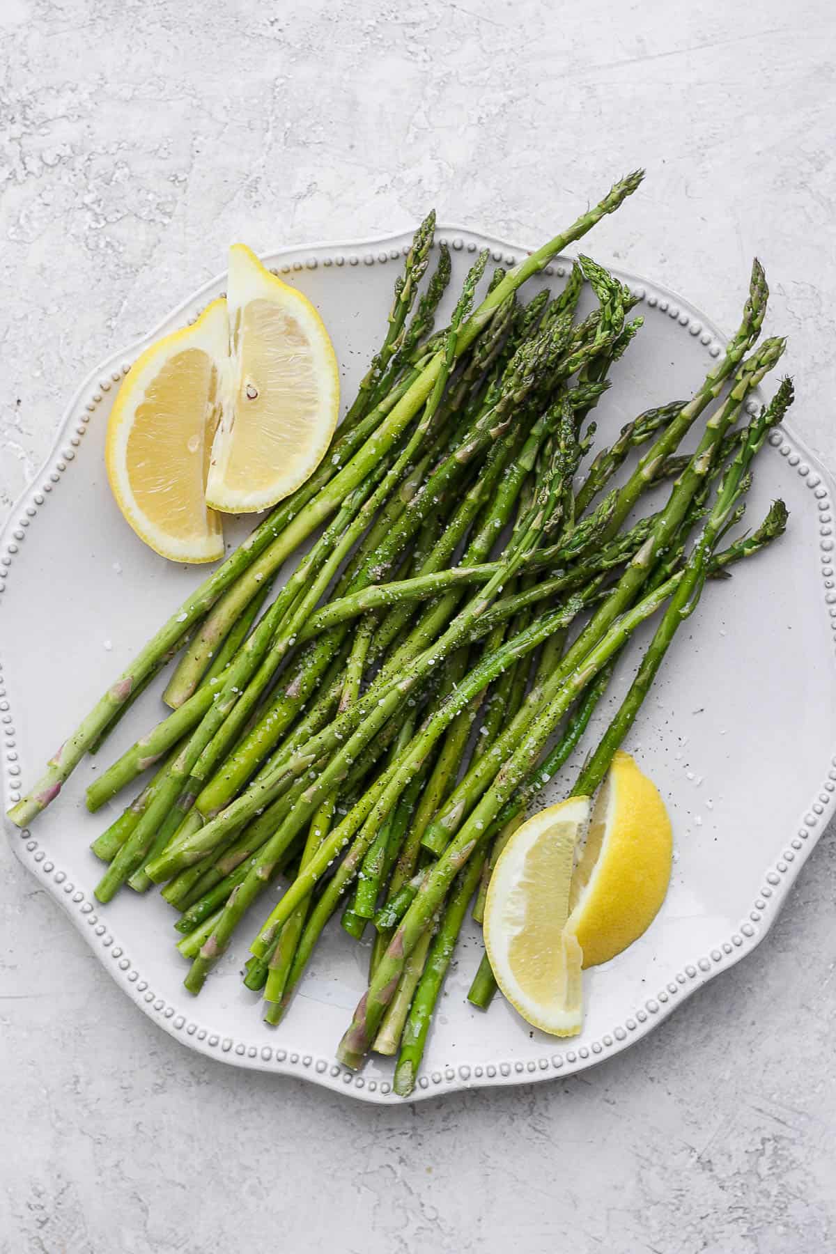 Oven roasted asparagus on a plate with lemon wedges