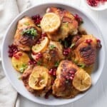 Pomegranate chicken thighs in a serving bowl with shallots, lemons, and garnish.