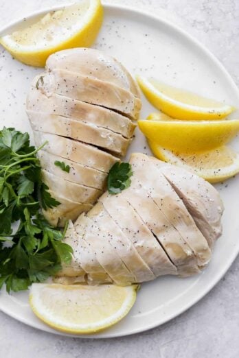 Poached chicken on plate with lemon slices and herbs