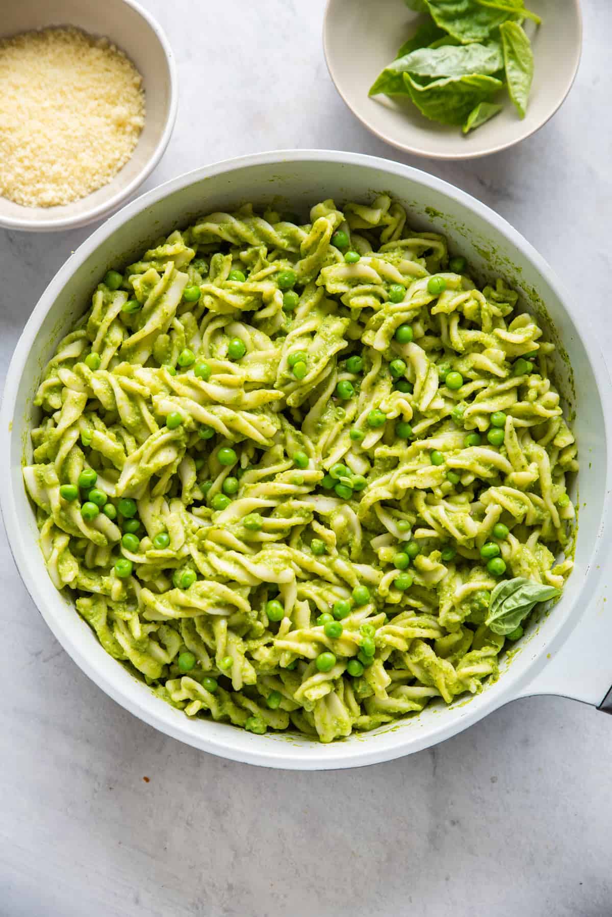 Large pot of pasta with peas with bowl of parmesan cheese and basil on the side