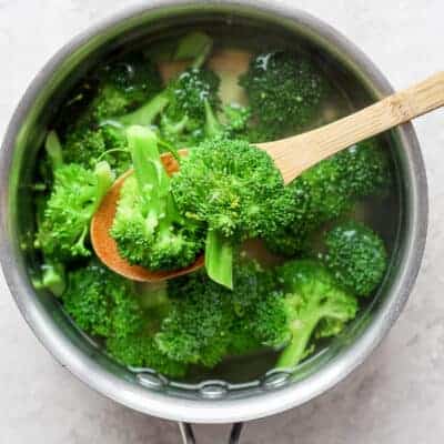 Cooked broccoli on slotted wooden spoon over pot of broccoli cooking