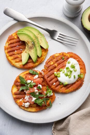 Three yogurt waffles on a plate with toppings added on top and fork on plate