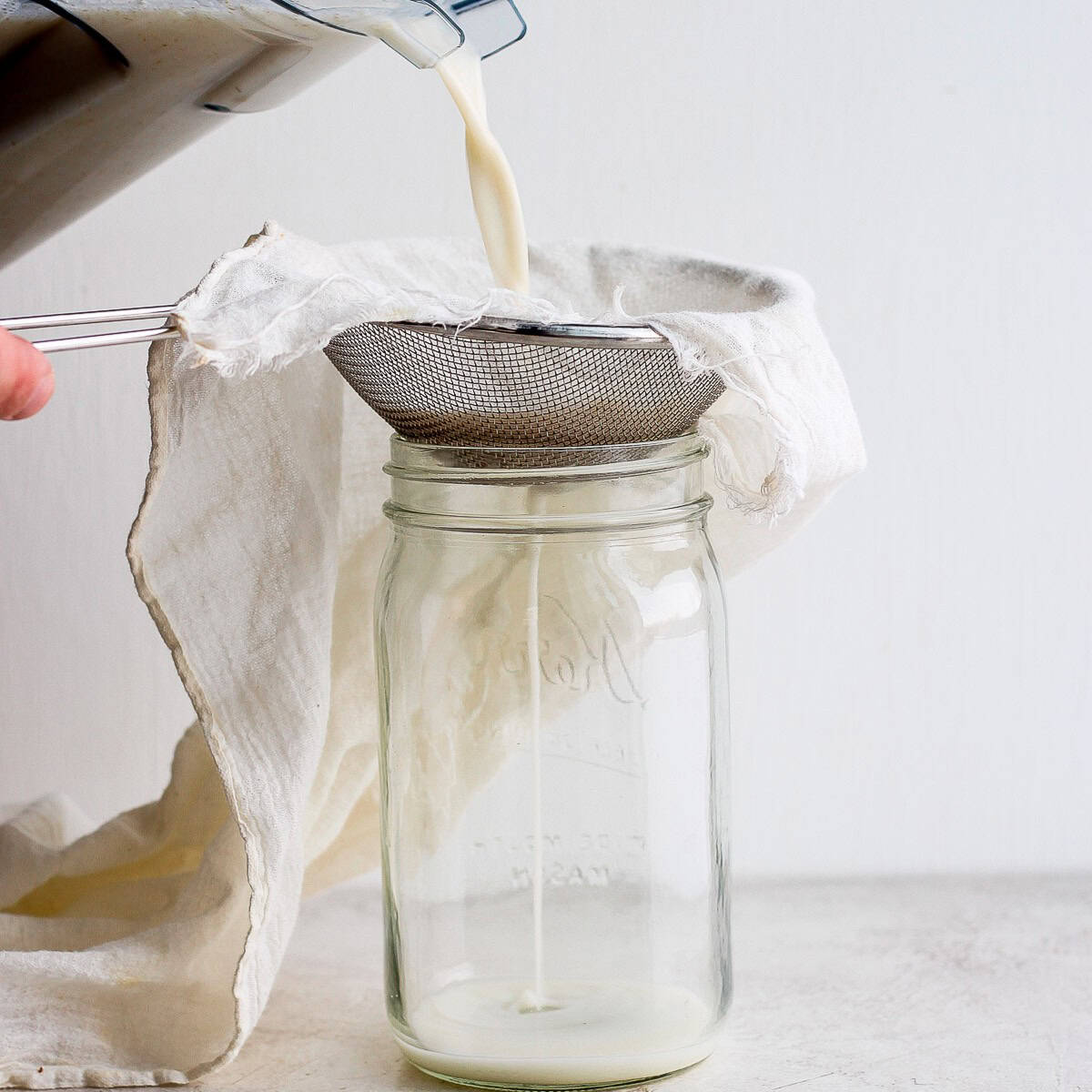 Oat milk being poured from the blender to a jar with a strainer on top.
