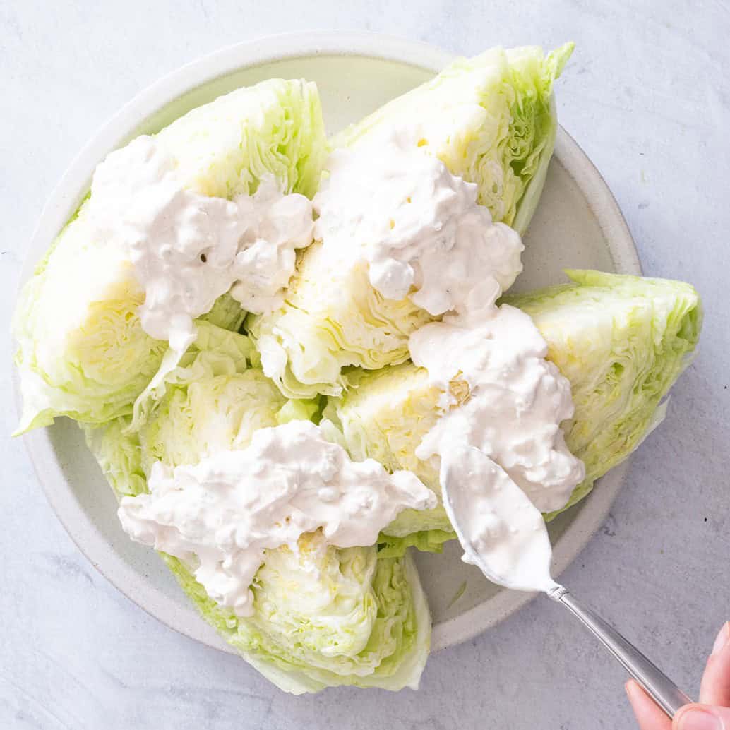 Dressing being poured onto the wedges of lettuce.