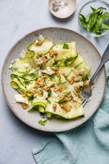 Large bowl of zucchini salad made with zucchini ribbons with blue towel and serving ware in bowl