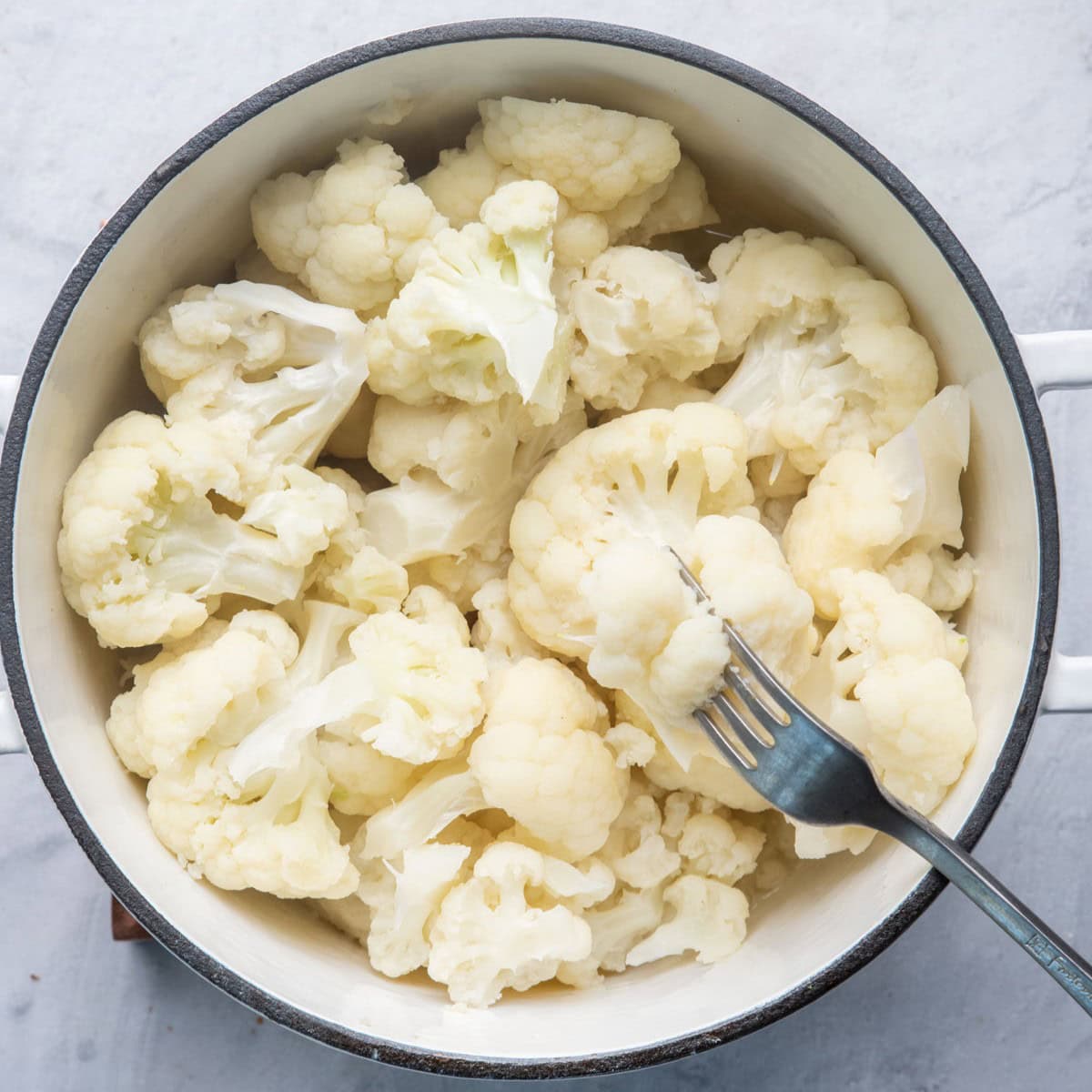 Cauliflower florets in pot after cooking with fork piecing.