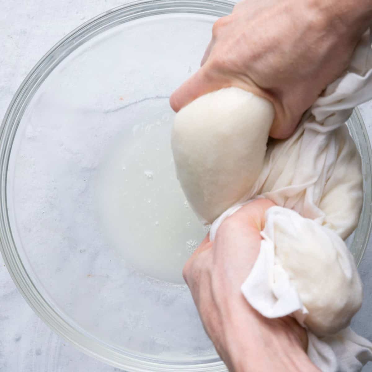 Squeezing out cauliflower water in kitchen cloth showing water dripping into bowl.