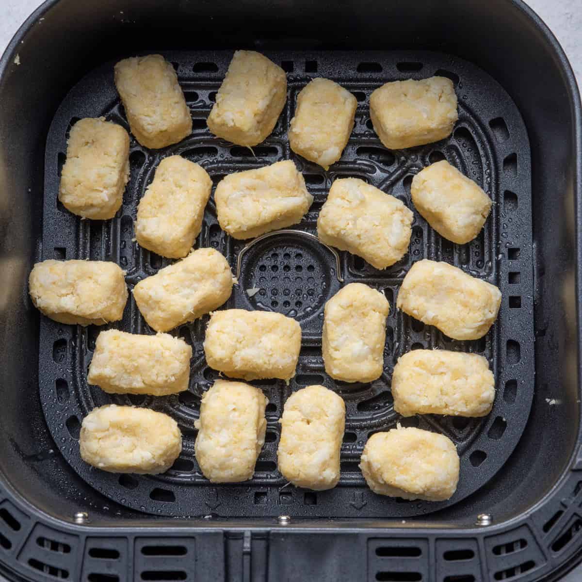 Cauliflower tots in air fryer basket before cooking.