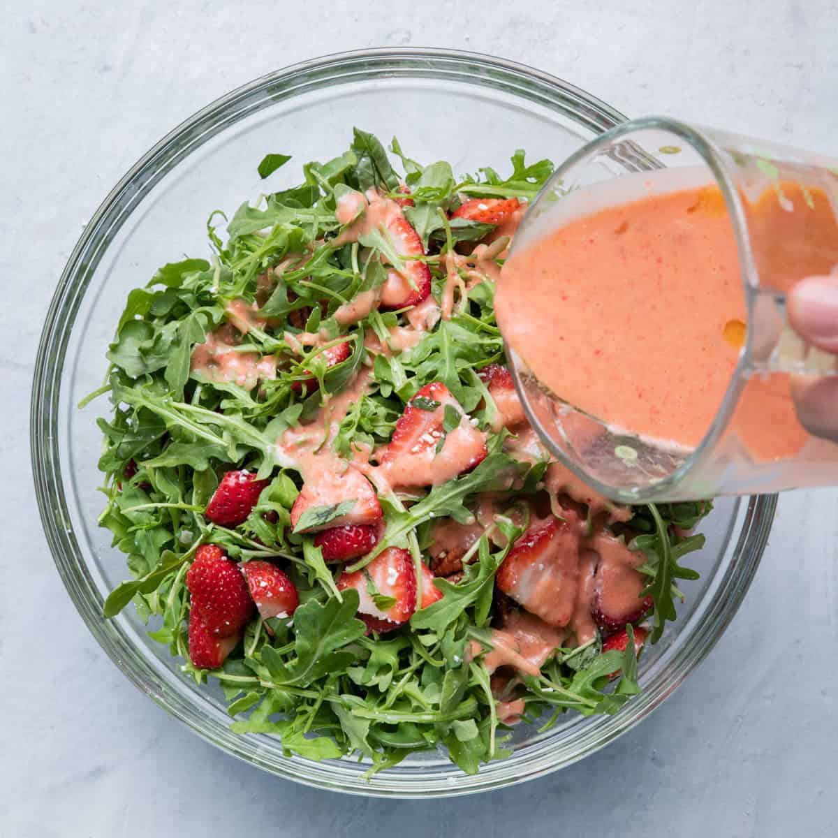 Pouring salad dressing over salad.