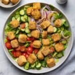 A bowl of feta salad with more ingredients nearby.