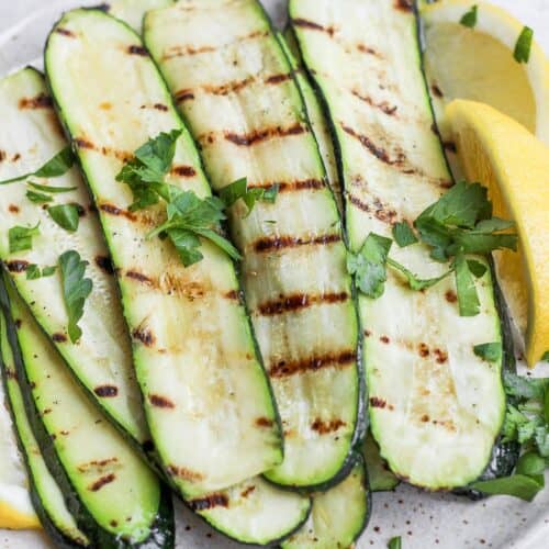 Grilled zucchini with lemon and garnish stacked on a plate.