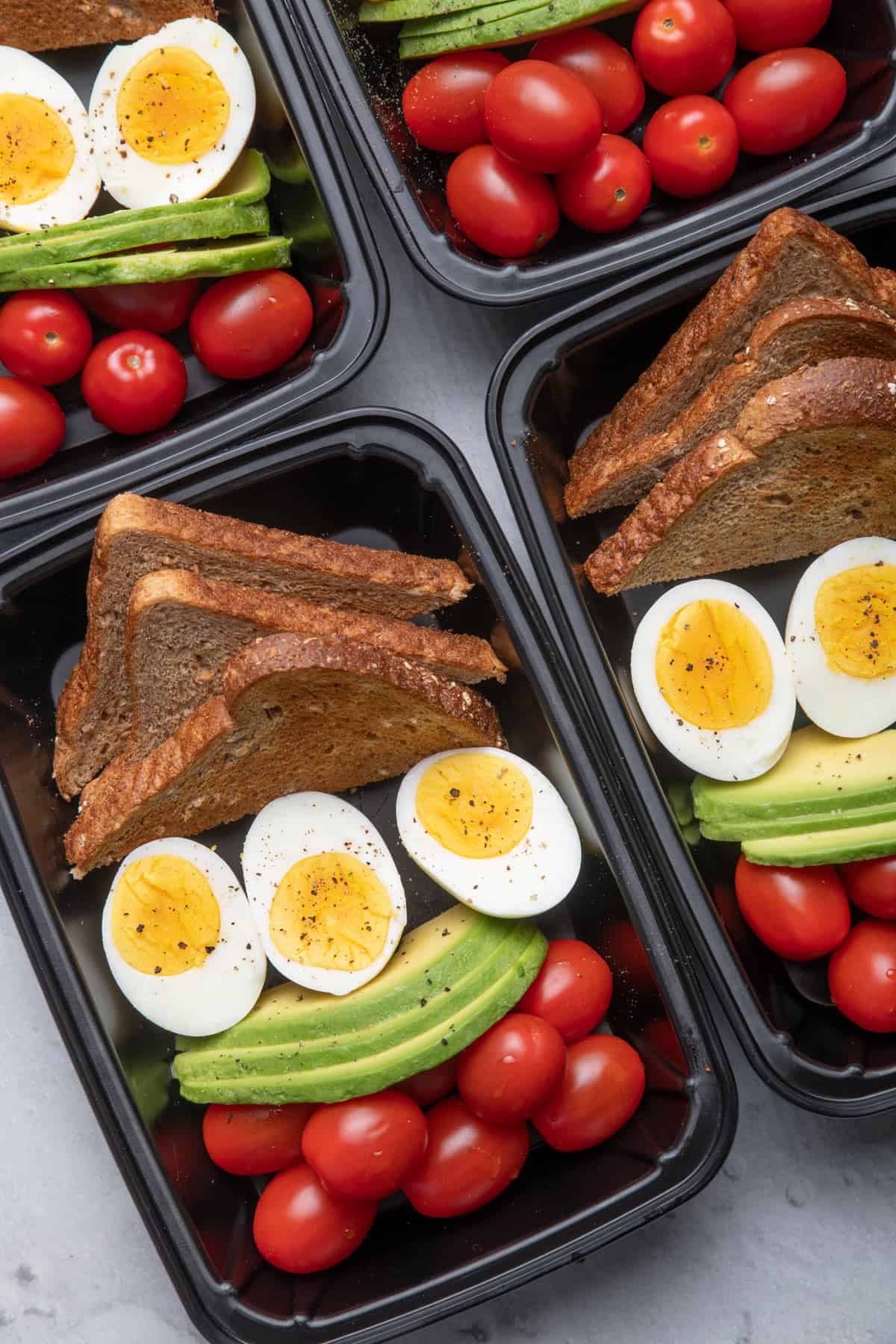 Meal prep containers with eggs, avocado, tomato and toast