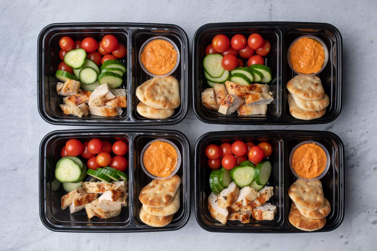 Grilled chicken and hummus meal prep containers with vegetables and naan bread